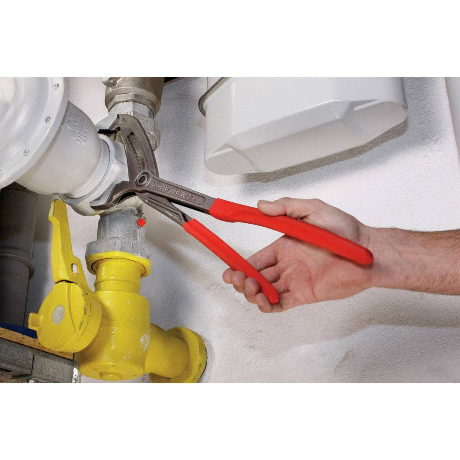 Eine Person verwendet Zangen mit roten Griffen, um ein weißes Rohr anzupassen, das mit einem gelben Ventil verbunden ist und wahrscheinlich Klempner- oder Wartungsarbeiten durchführt.