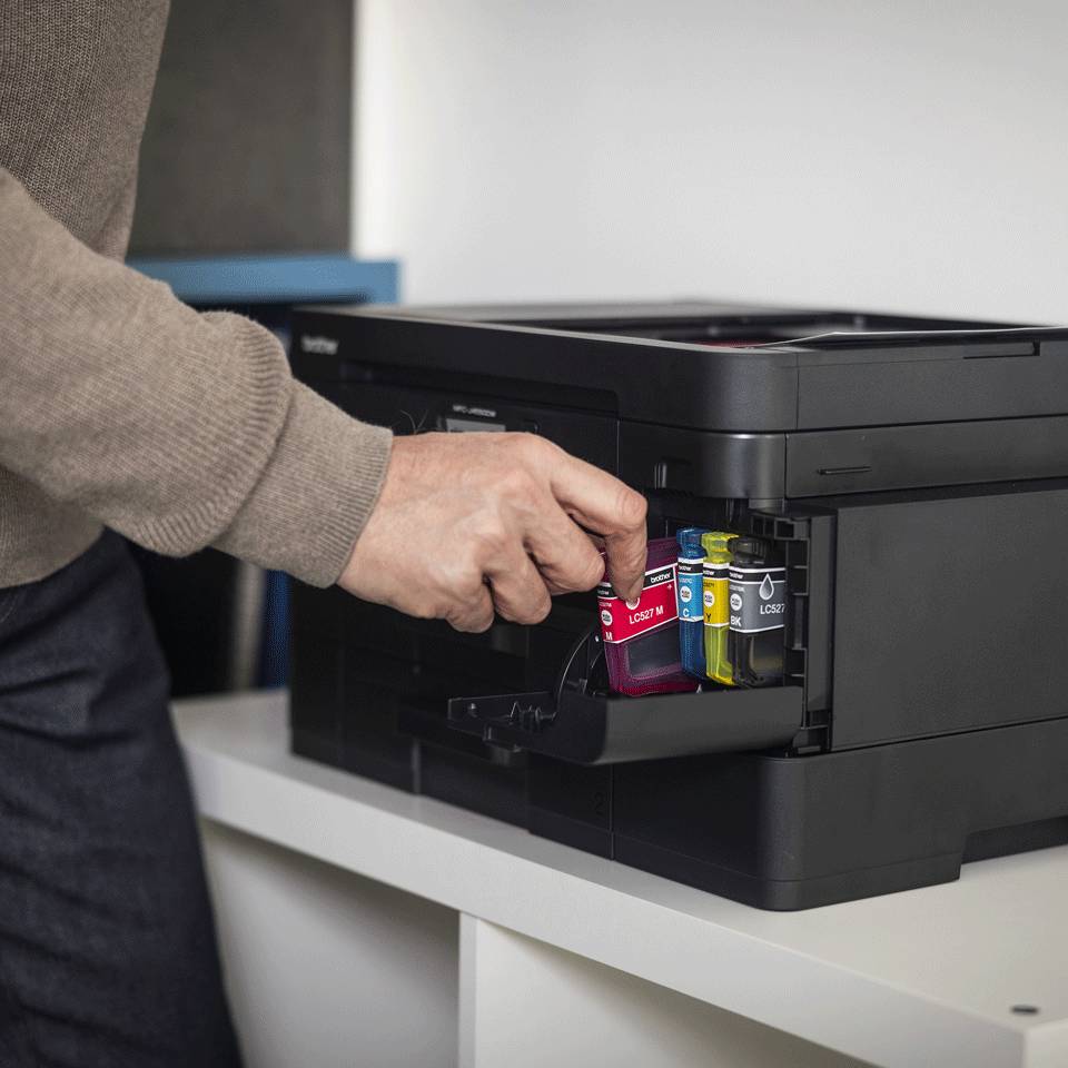 Person, die Tintenpatronen in einem schwarzen Drucker auf einem Schreibtisch austauscht.