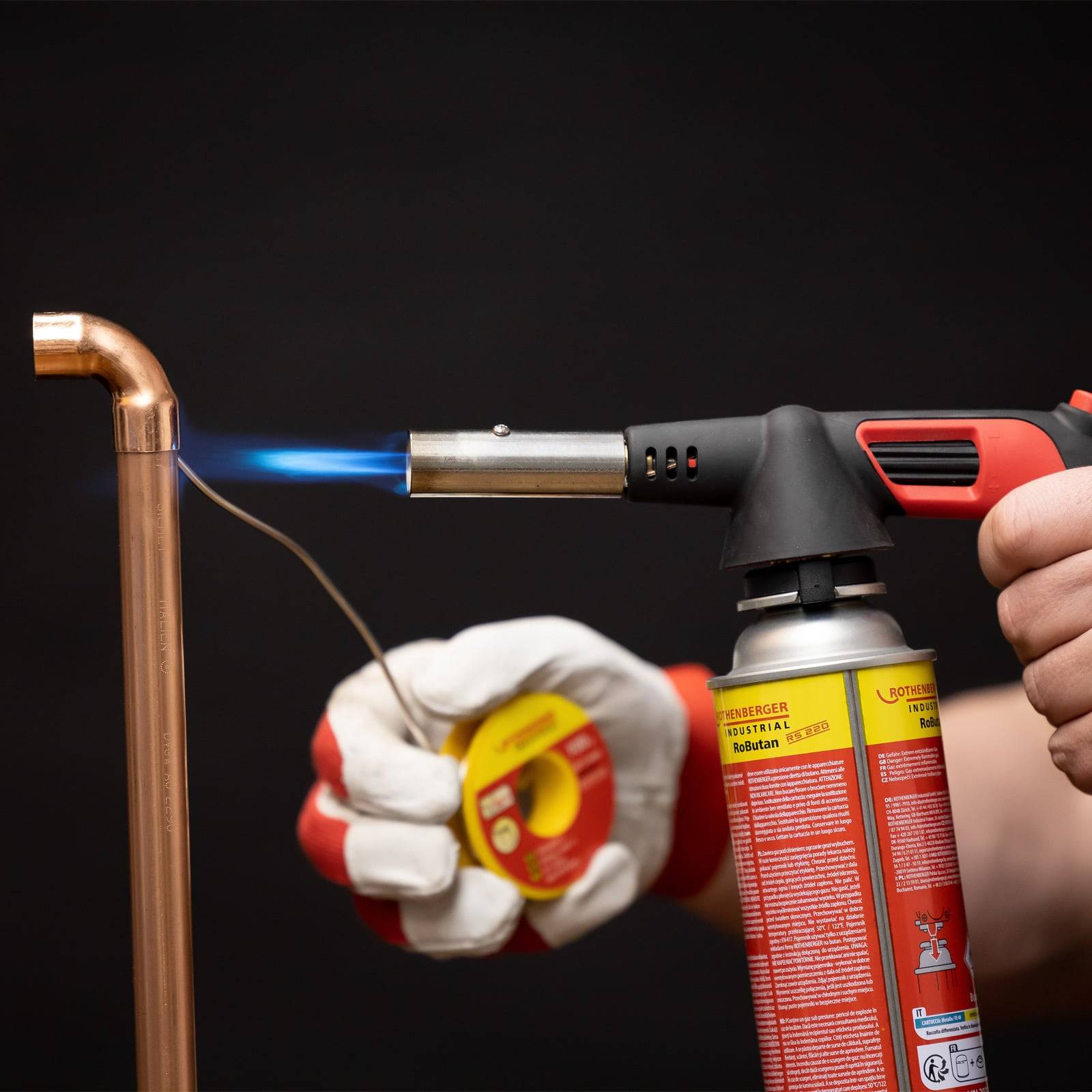 Eine Person verwendet einen tragbaren Lötbrenner, um ein Kupferrohr zu löten, was auf eine Klempner- oder Heimreparaturaufgabe hinweist.
