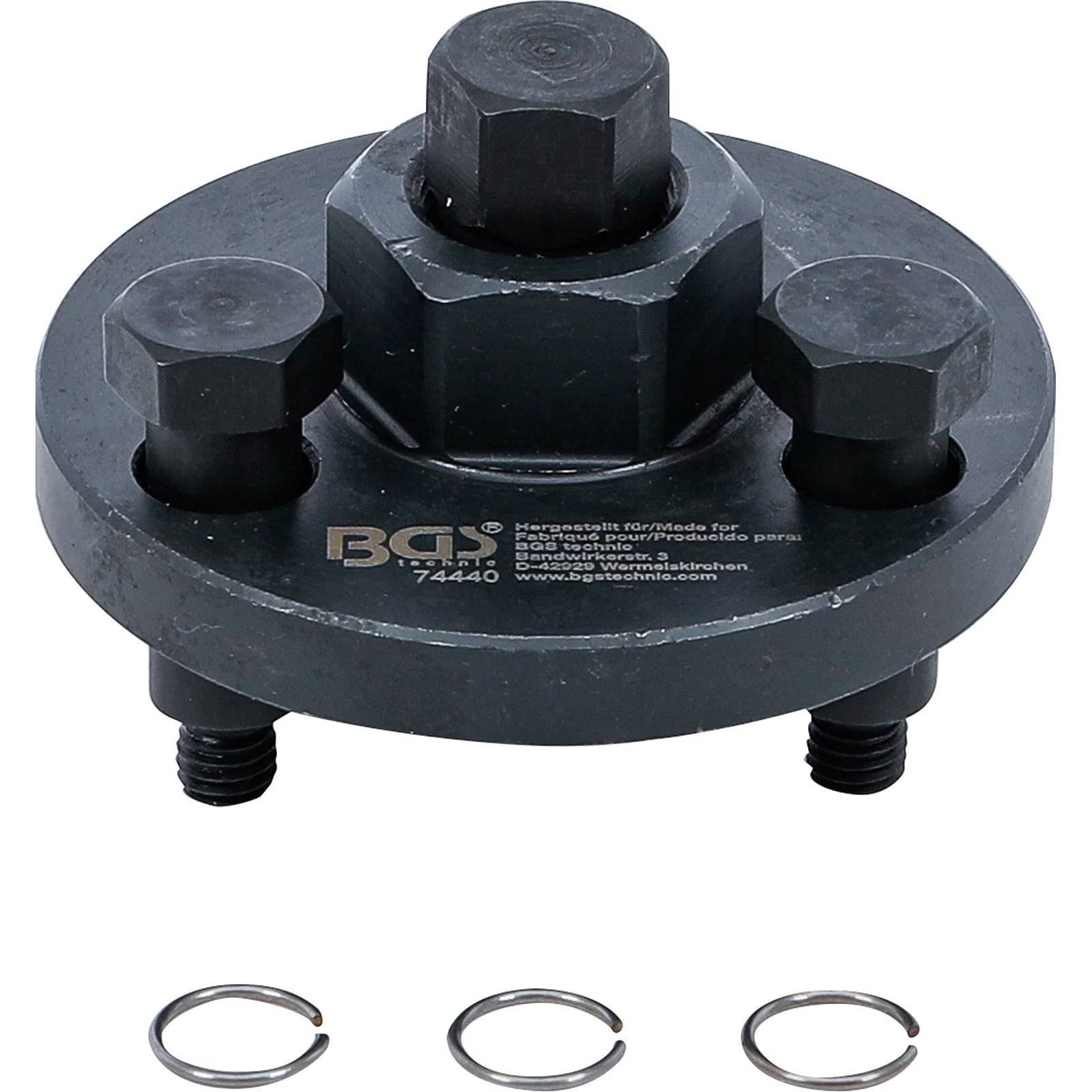 Ein kreisförmiges Metallwerkzeug mit drei verstellbaren Schrauben, beschriftet mit 'BGS 7444', das für mechanische Arbeiten verwendet wird und mit drei kleinen Metallringen präsentiert wird.
