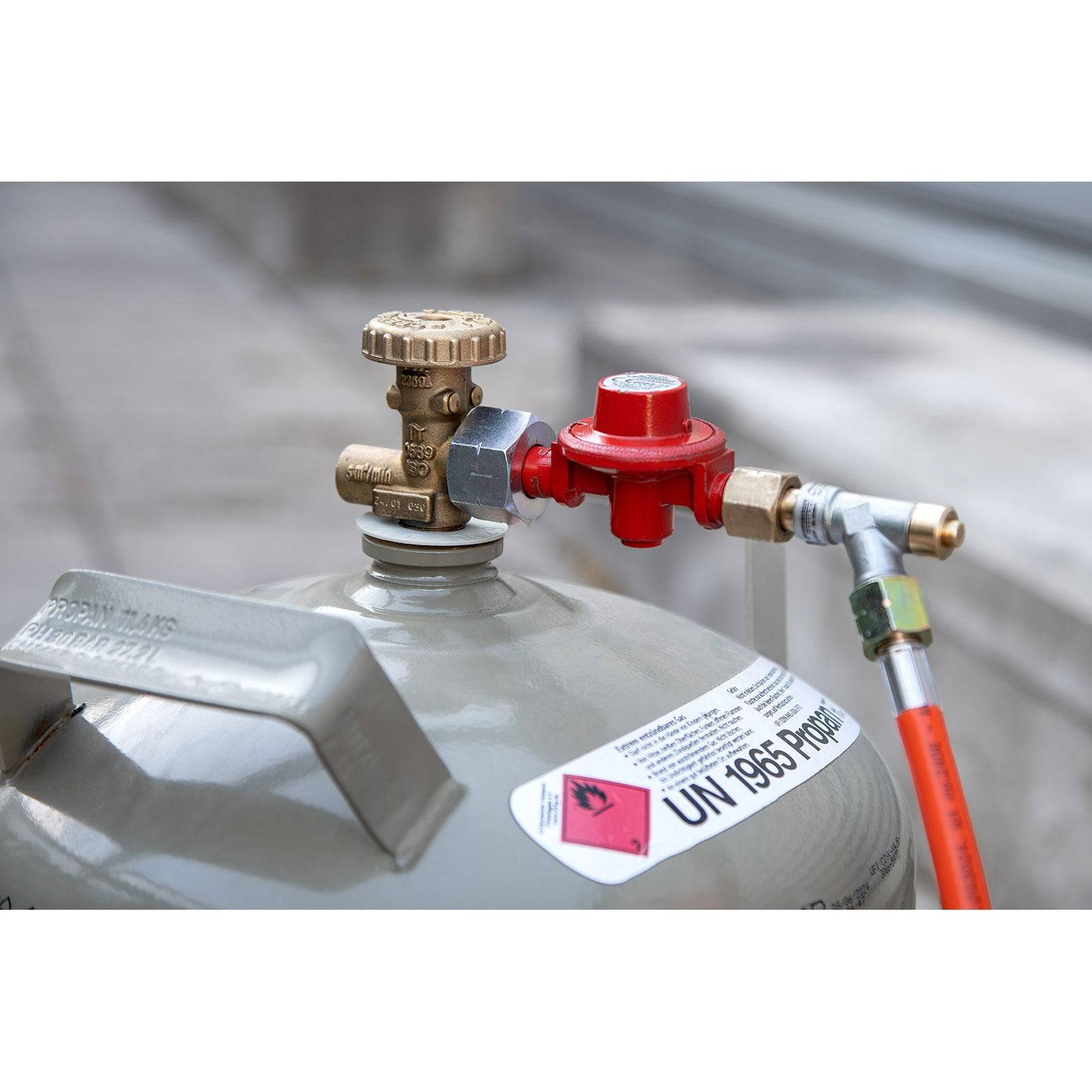„Eine Nahaufnahme einer Propangaszylinder mit einem Ventil und angeschlossenem roten Regler, beschriftet mit UN 1969 Propan, was die Inhalte kennzeichnet.
