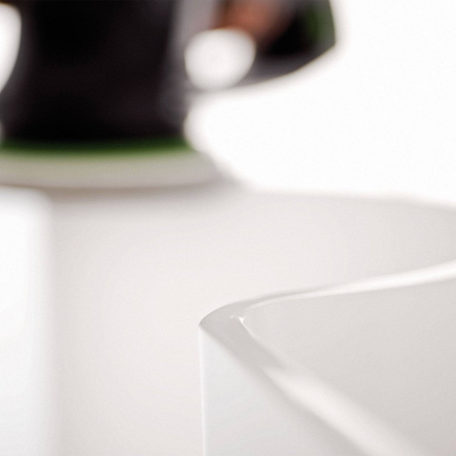 Eine Nahaufnahme von weißen Keramikkanten mit einem unscharfen Hintergrund, der einen Teil eines schwarzen Objekts mit grünem Detail zeigt, was auf ein modernes Design hindeutet.