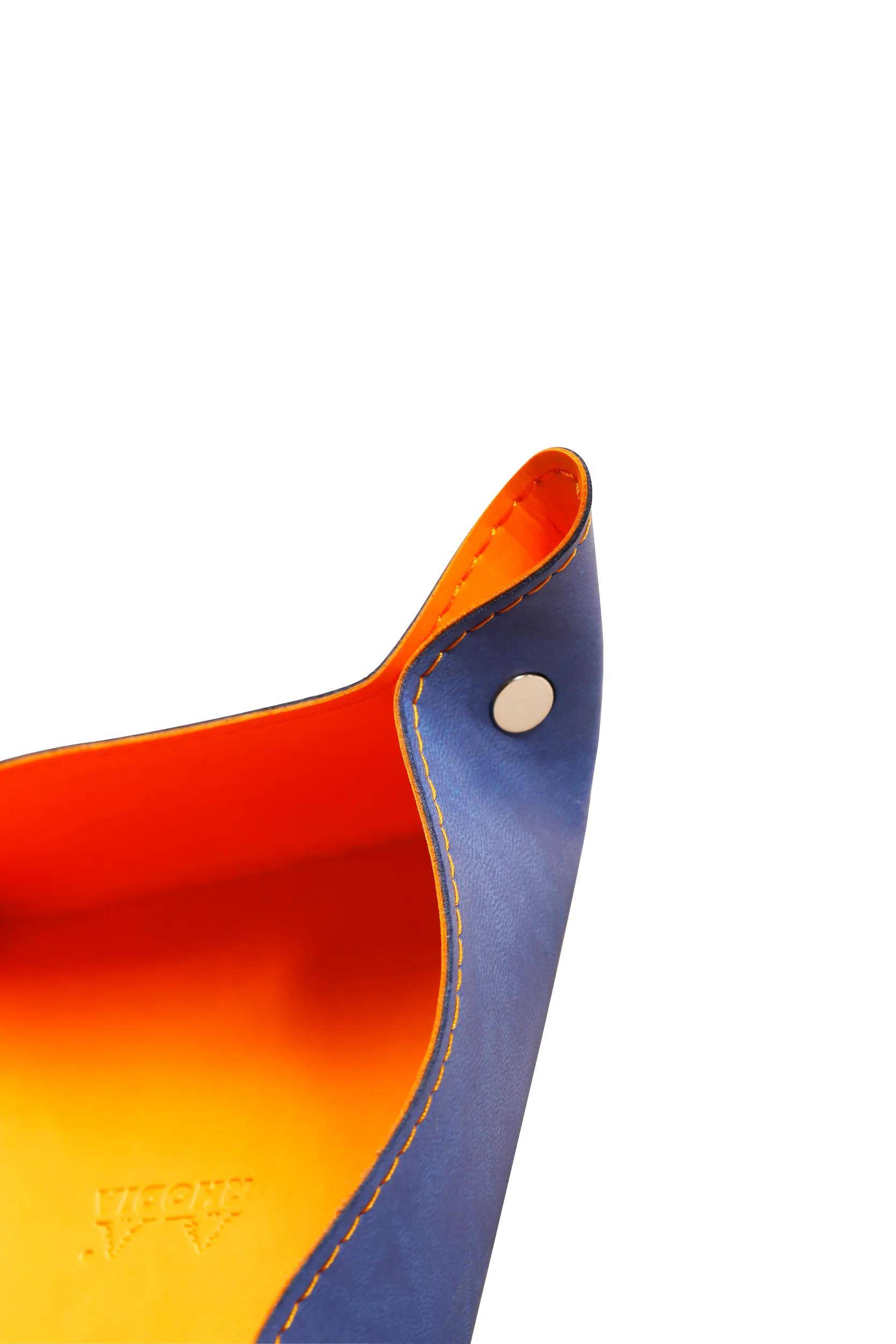 Eine Nahaufnahme einer orange- und blaulederfarbenen Tablett-Ecke, die deren Nähte und einen silbernen Druckknopf zeigt und die Handwerkskunst hervorhebt.