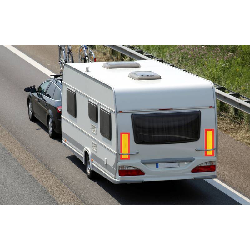 Ein Auto zieht einen weißen Wohnwagen auf einer Autobahn, mit Fahrrädern, die auf dem Dach des Autos montiert sind. Die Straße hat ein Metallgeländer und einen grasigen Seitenstreifen.