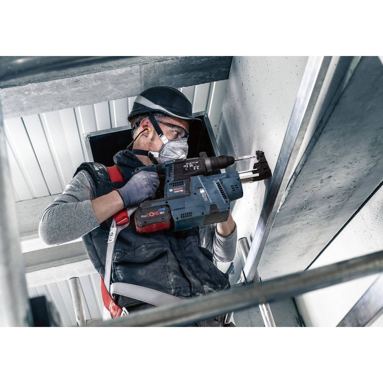 Ein Bauarbeiter in Schutzausrüstung verwendet einen Elektroschrauber an einer Betonwand, was auf aktive Arbeiten in einer Bauumgebung hinweist.