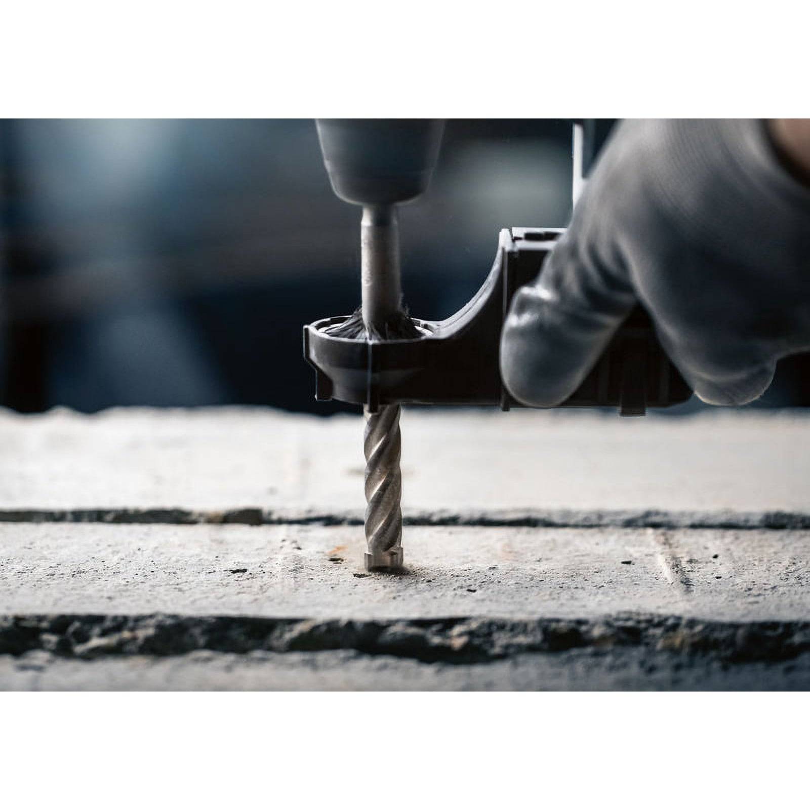 Eine behandschuhte Hand bedient einen Elektroschrauber und bohrt in eine Betonoberfläche, wobei Staubpartikel entstehen. Das Bild zeigt Bauarbeiten.