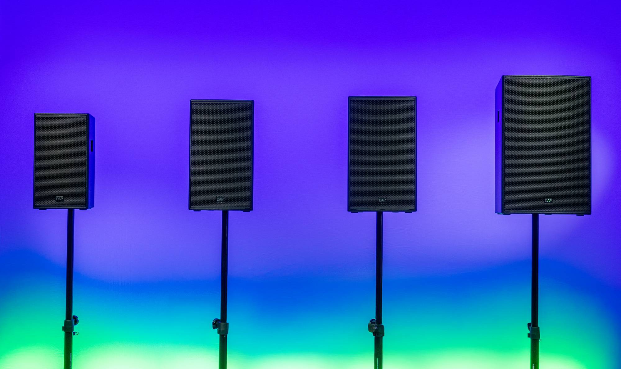 Zwei schwarze Lautsprecher auf Ständern vor einem lebendigen Hintergrund mit Farbverlauf von Blau zu Violett, der eine dynamische Atmosphäre schafft.
