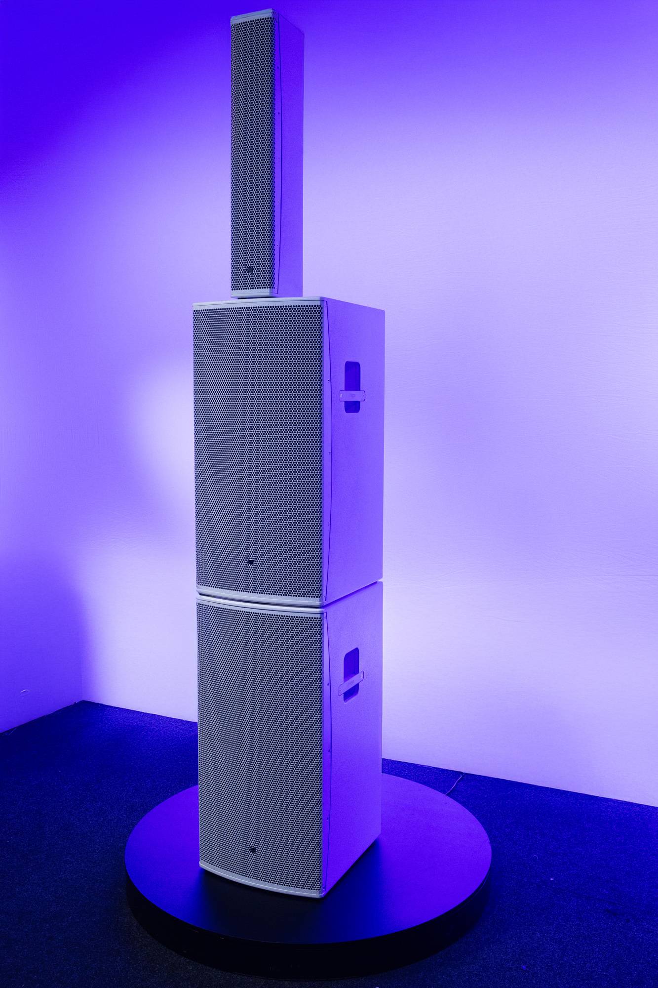Ein hoher, rechteckiger Lautsprecher mit einem kleineren Lautsprecher oben, vor einem lila beleuchteten Hintergrund.