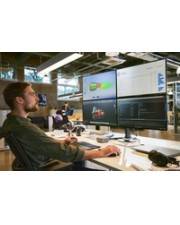 Eine Person in einer Büroumgebung arbeitet an einem Computer mit mehreren Bildschirmen, auf denen verschiedene Software und Daten angezeigt werden, was auf eine technisch orientierte Aufgabe hindeutet.