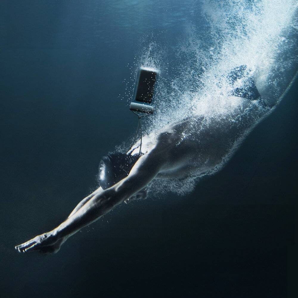 Eine Person taucht unter Wasser ab, während sie ein Smartphone hält, das über ihr schwebt. Die Szene ist mit einem blauen Farbton beleuchtet, was tiefes Wasser andeutet.