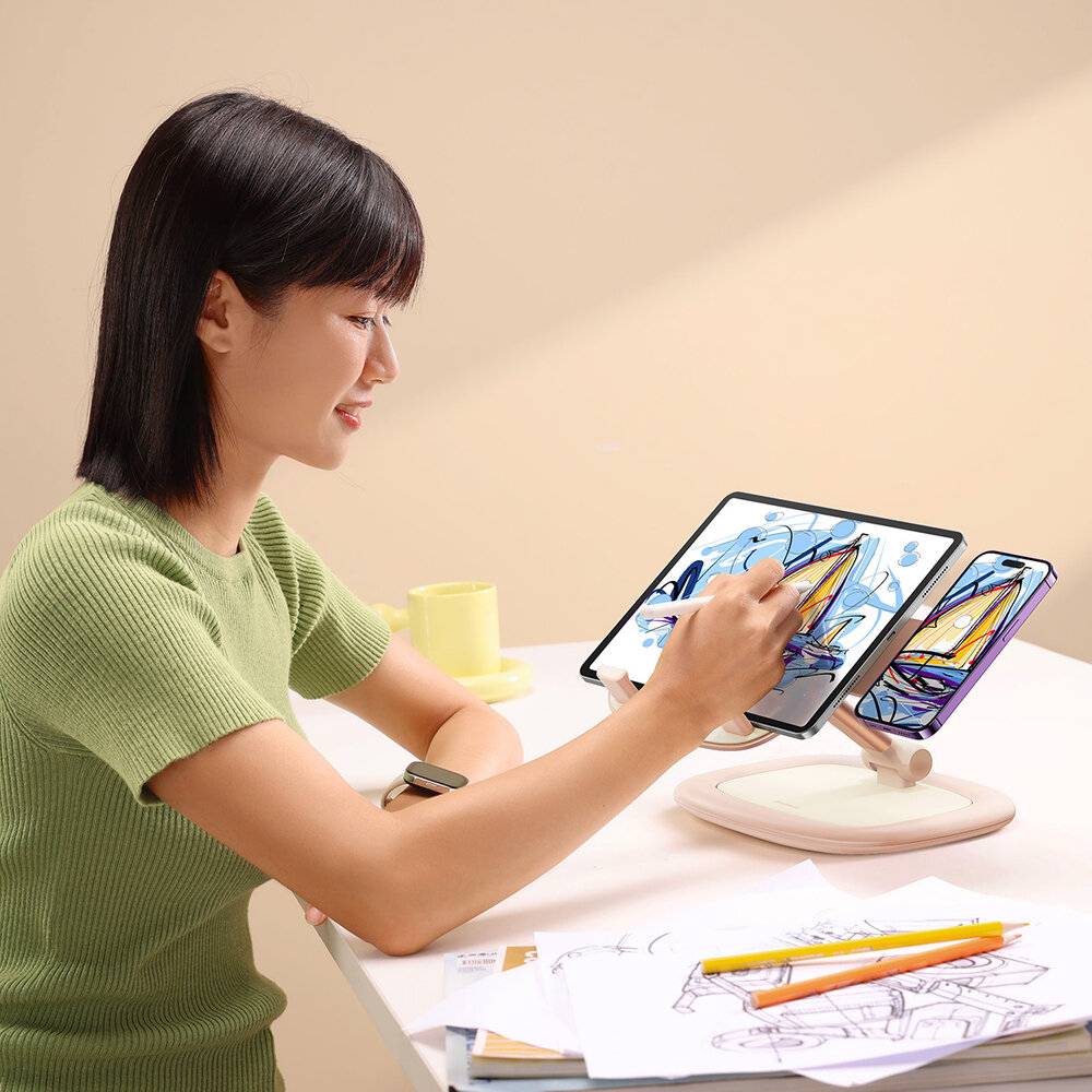 Eine Person sitzt an einem Schreibtisch und zeichnet mit einem Stylus auf einem digitalen Tablet. Der Schreibtisch ist mit Papieren, Bleistiften und einer Tasse ausgestattet, was auf einen kreativen Arbeitsplatz hindeutet.