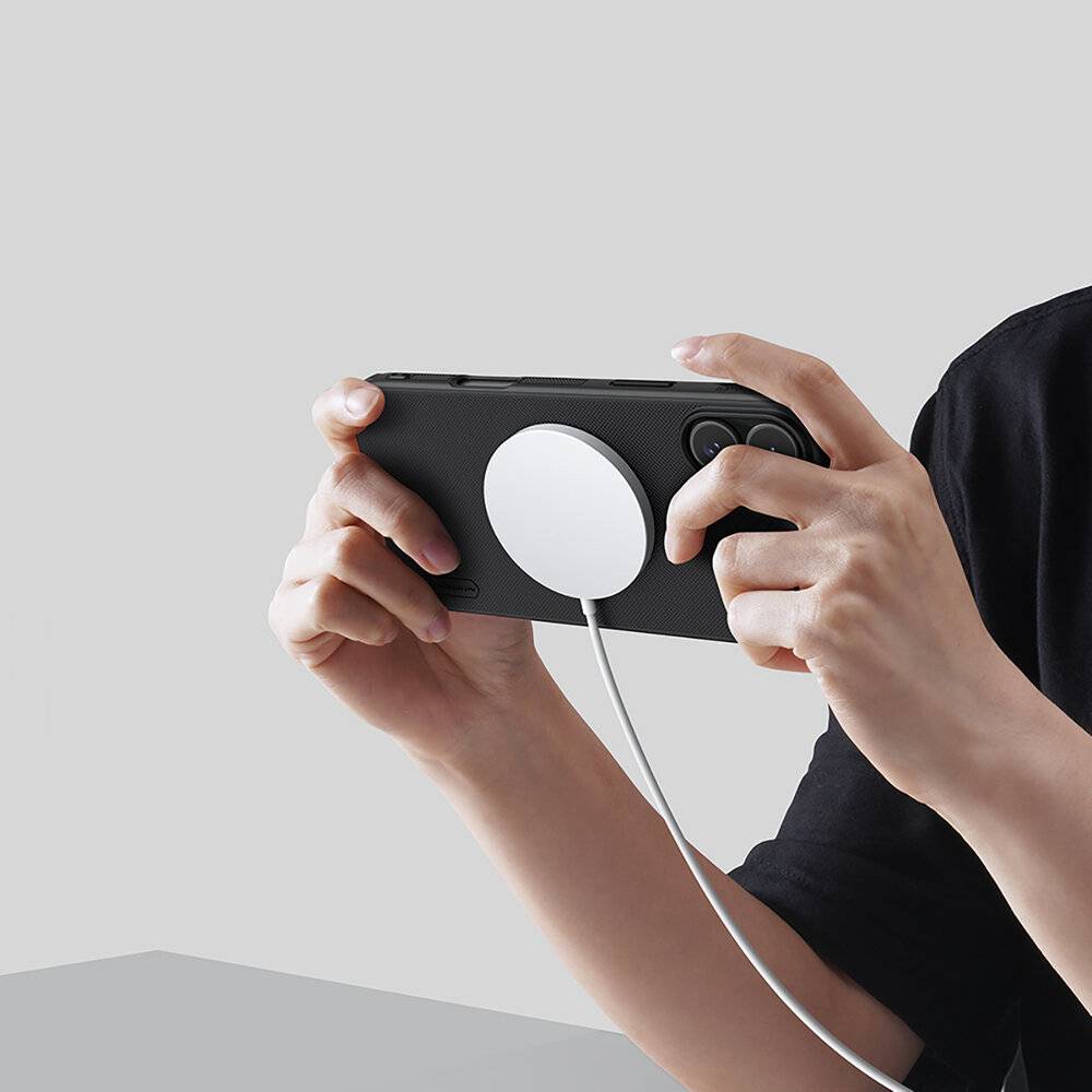 Eine Person hält ein Smartphone horizontal in den Händen, während ein rundes magnetisches Ladegerät auf seiner Rückseite für kabelloses Laden angebracht ist.