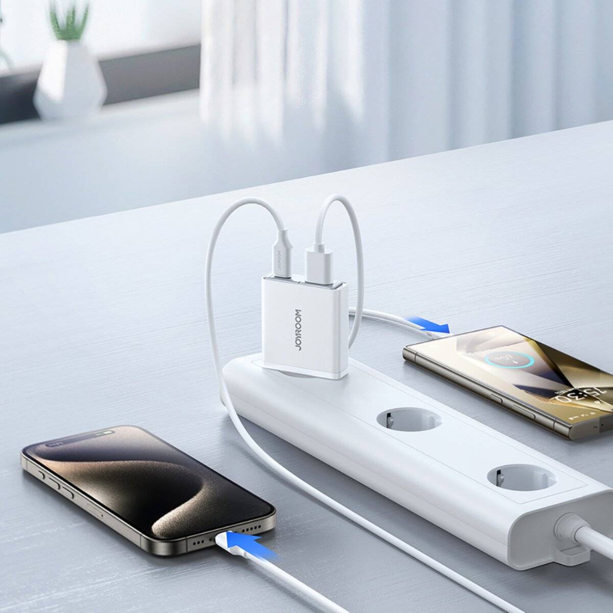 Ein Smartphone, das an einer weißen Steckdosenleiste mit einem Dual-Port-Wandladegerät auflädt; ein anderes Handy liegt in der Nähe und unterstreicht die Ladeeinrichtung.