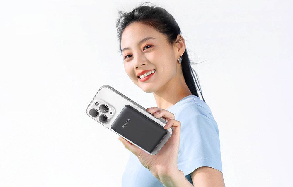 Eine Person in einem hellblauen Hemd hält ein Smartphone mit einem kleinen, angebrachten Gerät mit der Bezeichnung „MAGCOST