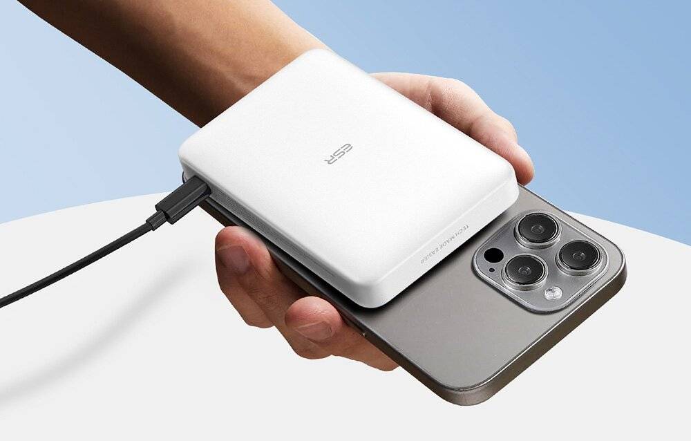 Eine Person hält ein Smartphone mit einer weißen ESR-Powerbank, die auf der Rückseite angebracht ist, und lädt das Gerät drahtlos auf einem hellen Hintergrund auf.