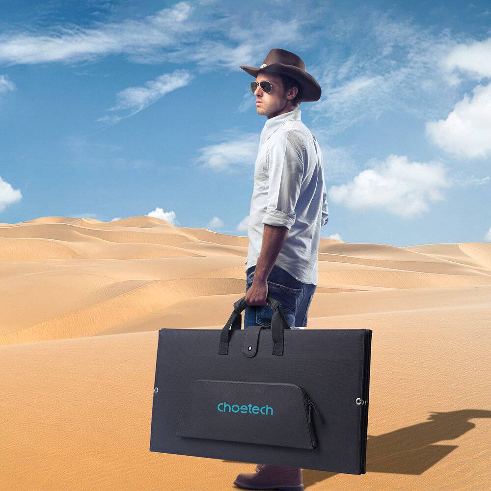 Eine Person mit Hut und Sonnenbrille steht in einer Wüste und hält einen großen schwarzen Chosetech-Solarpanelkoffer, mit Sanddünen im Hintergrund.