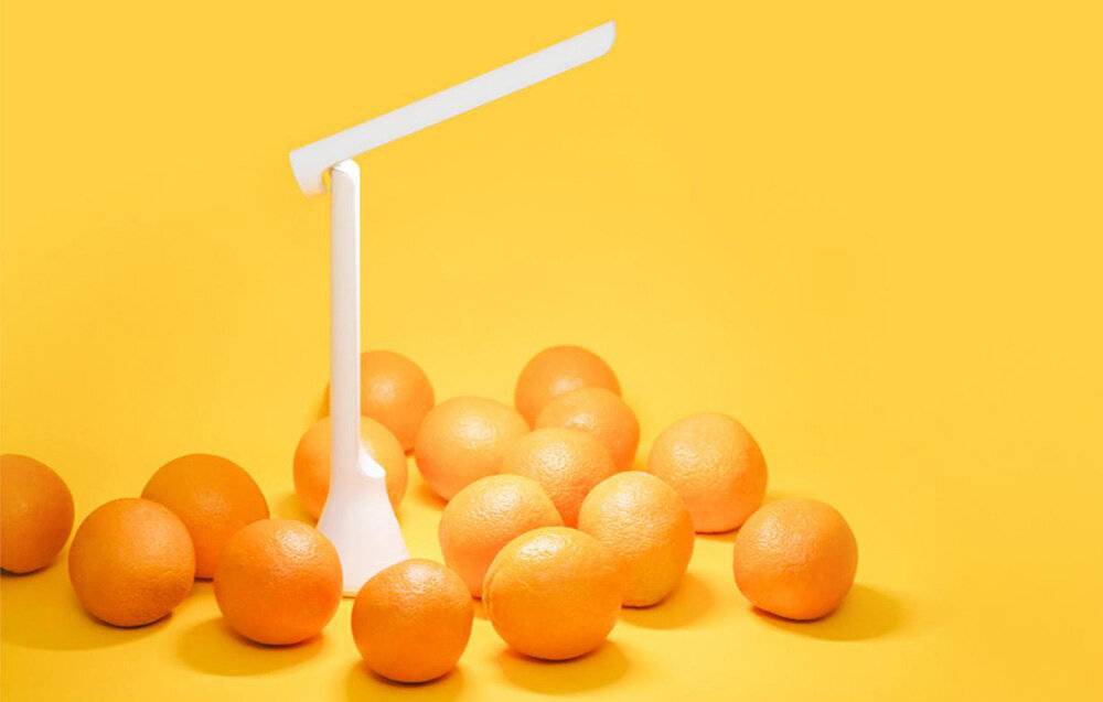 Eine moderne weiße Schreibtischlampe steht inmitten von verstreuten Orangen auf hellorangen Hintergrund.