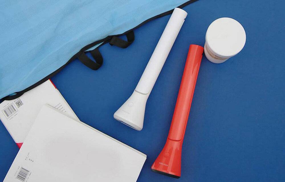 Rot-weiße tragbare Handventilatoren auf einer blauen Oberfläche neben einem cremefarbenen runden Behälter und einem offenen Notizbuch.