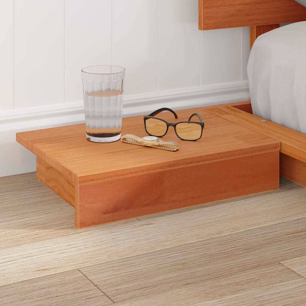 Ein hölzernes Nachttischregal mit einem Glas Wasser und einer Brille steht neben einem Bett in einem Raum mit hellem Holzboden.