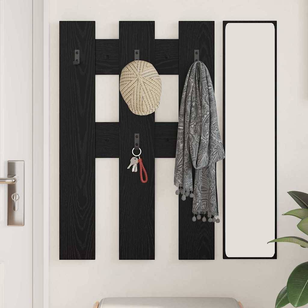 Ein schwarzes, an der Wand montiertes Garderobenregal mit drei Haken, an denen ein Strohhut, ein Schlüsselbund und ein gemusterter Schal hängen, neben einem hohen, schmalen Spiegel.