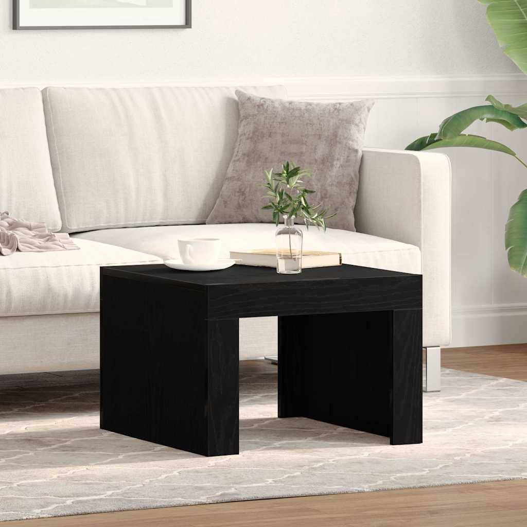Ein modernes Wohnzimmer mit einem weißen Sofa, grauen Kissen, einem kleinen schwarzen Couchtisch, auf dem ein Buch und eine Pflanze stehen, neben einem hellen Teppich auf Holzboden.