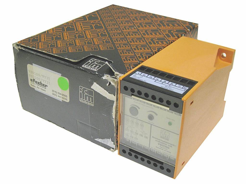 Ein industrielles elektronisches Modul in einem abgenutzten Karton, mit gelb-oranger Frontplatte und einer teilweise sichtbaren, beschrifteten Bedienoberfläche.