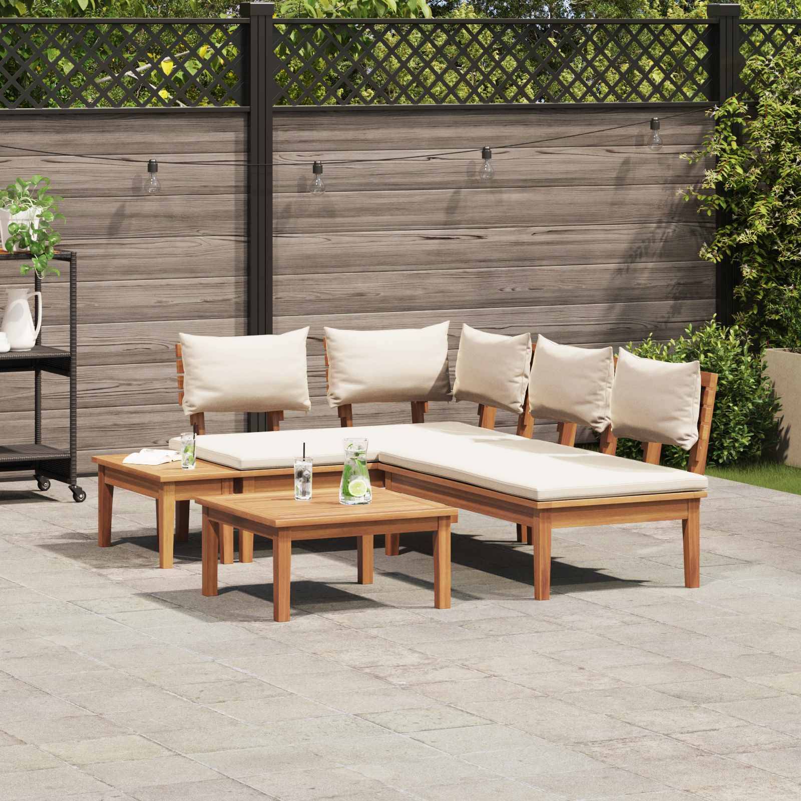 Terrasse im Freien mit Holzmöbelset, bestehend aus einem Sofa, einer Liege und Tischen; im Hintergrund sind ein Holzzaun und Pflanzen zu sehen.
