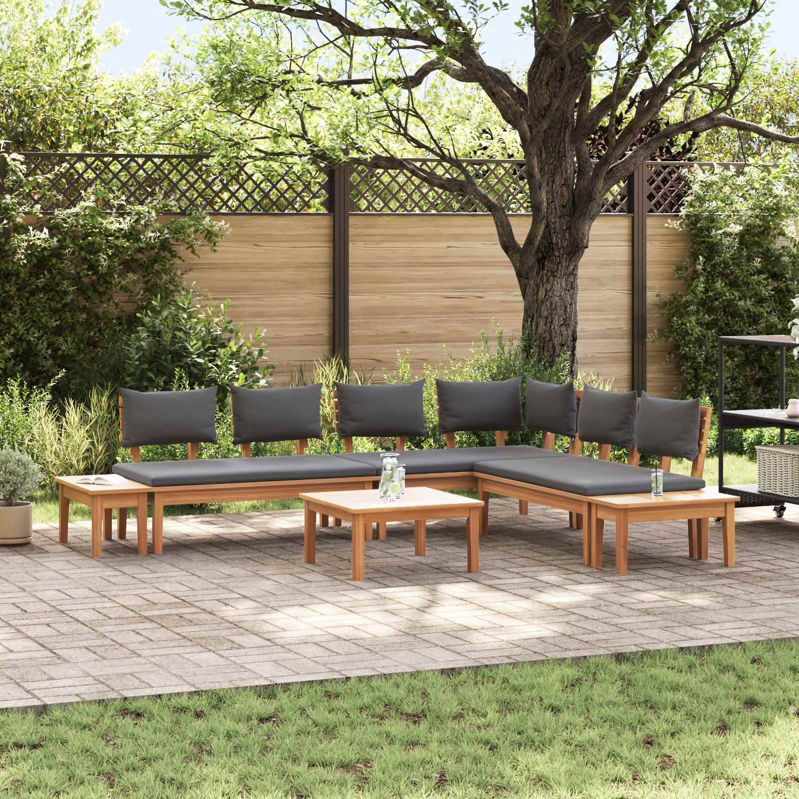 Eine Terrasse mit einem L-förmigen Holzsofa und Kissen, einem kleinen Couchtisch und Topfpflanzen, die vor einem Holzzaun und Bäumen platziert sind.