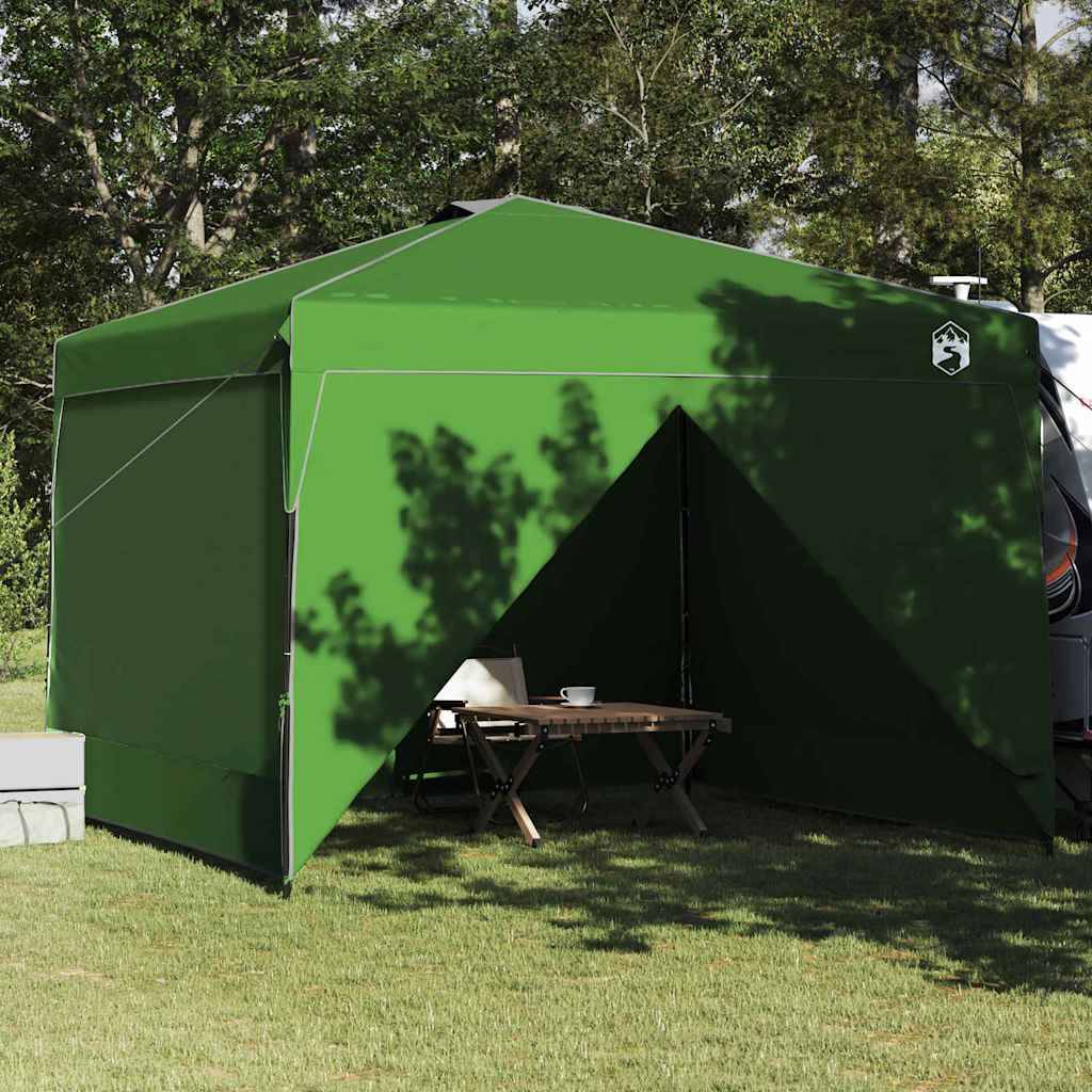 Ein grünes Zelt mit einem offenen Eingang steht in einem bewaldeten Gebiet. Ein kleiner Tisch und zwei Stühle befinden sich im Inneren und deuten auf einen Campingplatz-Aufbau hin.