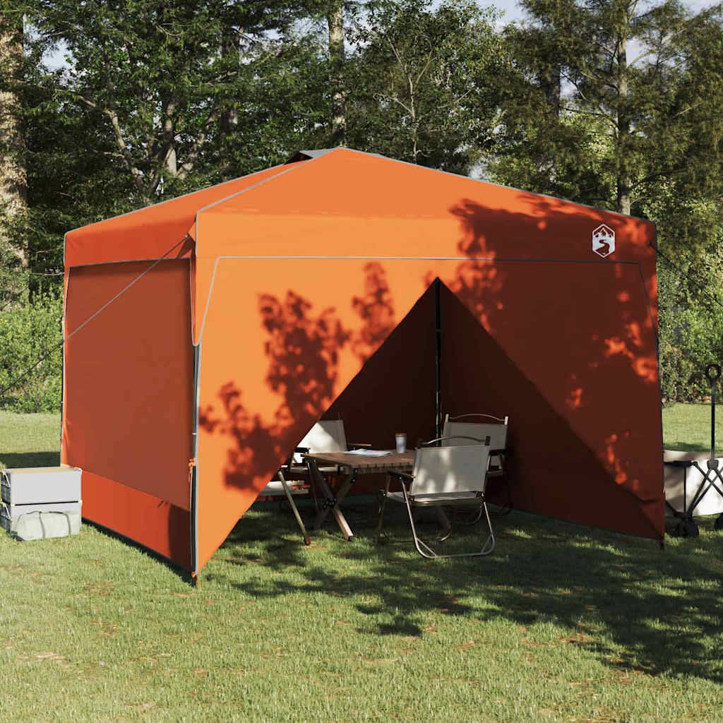 Ein orangefarbenes Outdoor-Pavillon-Zelt ist auf Gras aufgebaut und bietet Schatten für einen Tisch und Stühle darunter, umgeben von Bäumen.