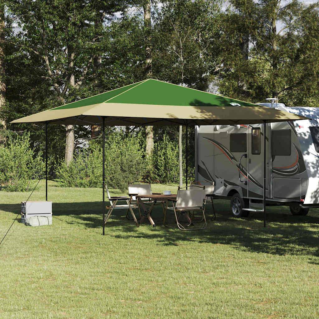 Ein Mobilheim steht auf Gras mit einem grünen Pavillon, der einen Picknicktisch und Stühle im Schatten bietet, vor einer Baumkulisse.