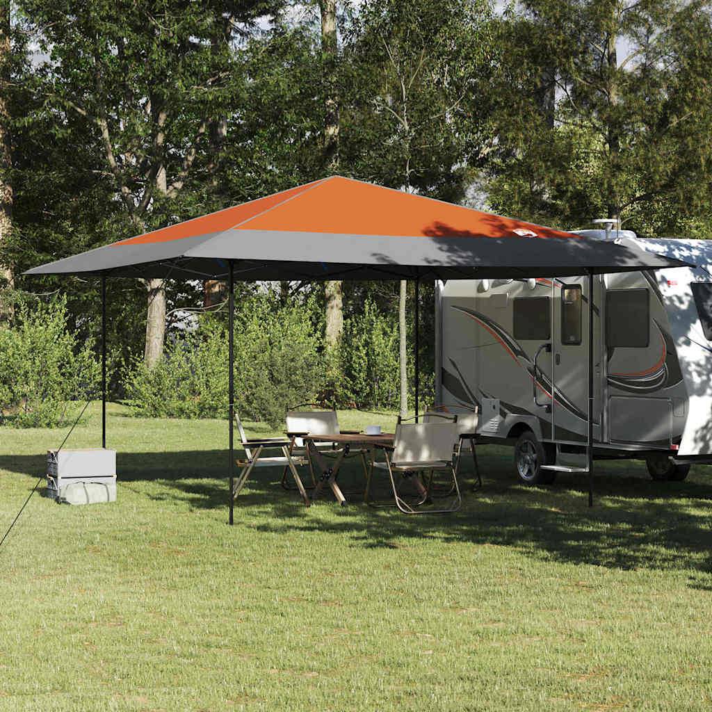 Ein geparkter Wohnmobil mit einem ausgefahrenen orange-grauen Markise, Campingstühlen und einem Tisch daneben, umgeben von Bäumen und Grünpflanzen.