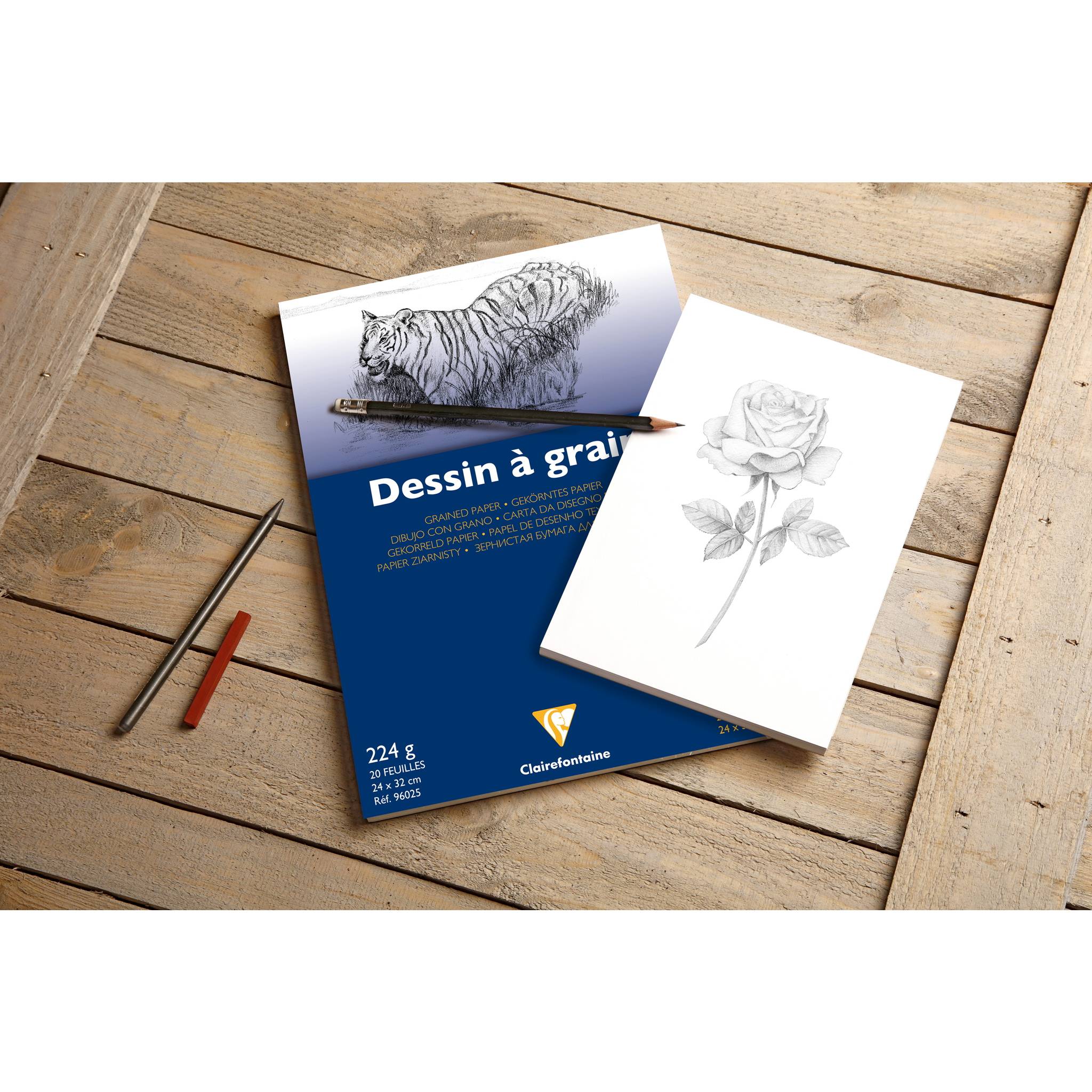 Skizzenbuch mit der Aufschrift "Dessin à grain"" auf einem Holztisch mit einem Bleistift, Kohlestifte und Beispielzeichnungen eines Tigers und einer Rose.