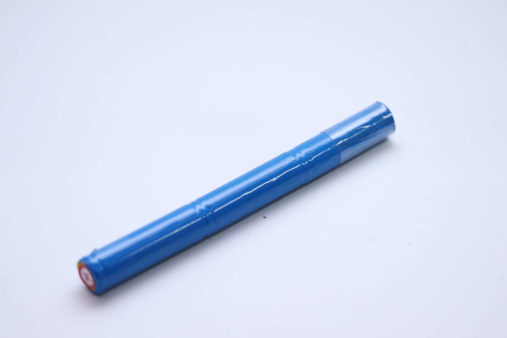 Eine blaue Lithium-Ionen-Batterie liegt auf einer weißen Oberfläche, zylindrisch geformt mit einer glänzenden Außenseite, was darauf hindeutet, dass sie neu und unbenutzt ist.