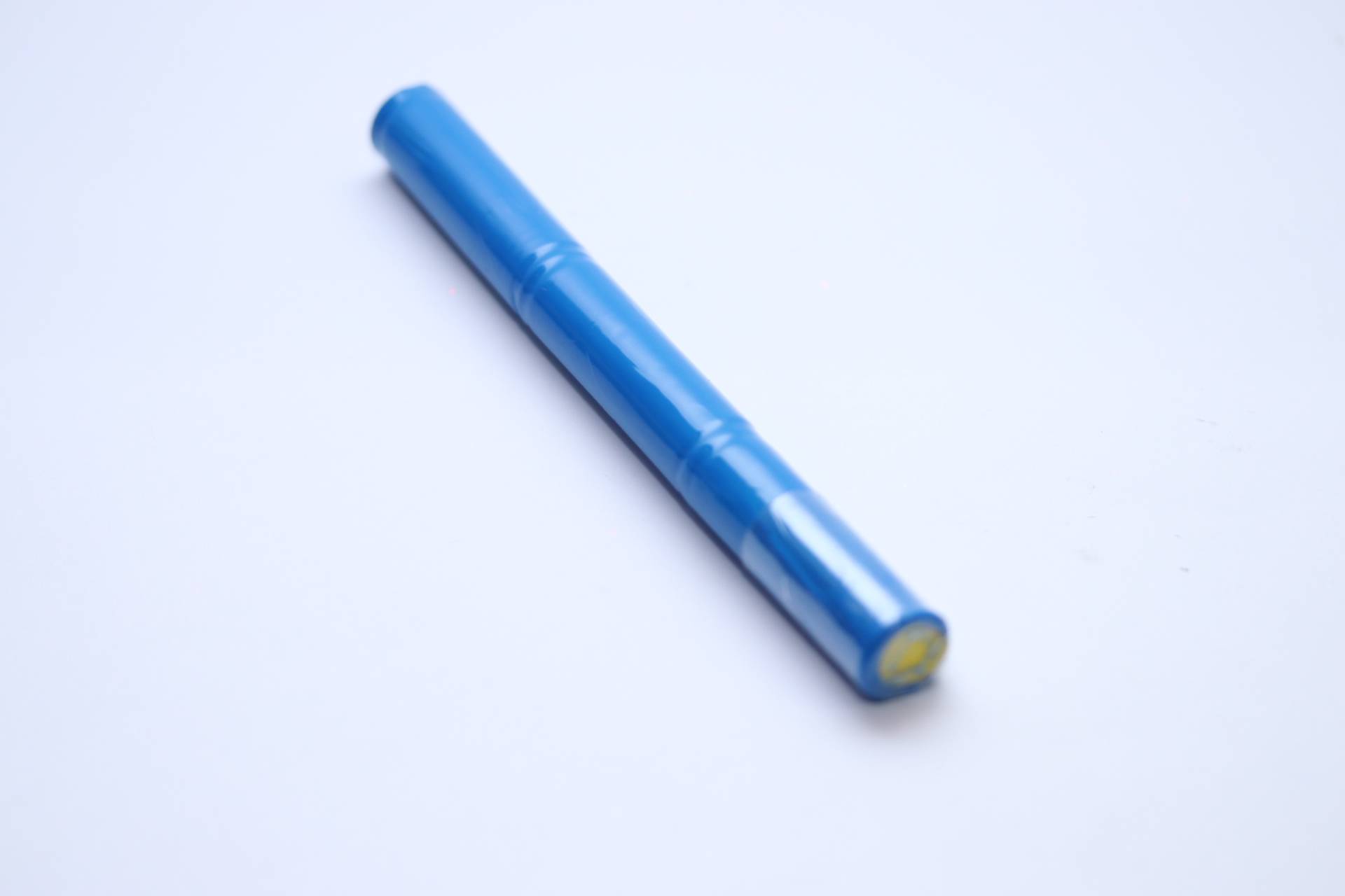 Ein blauer zylindrischer Stift liegt diagonal auf einer schlichten weißen Oberfläche und zeigt seine Einfachheit und strömungsoptimierte Gestaltung.