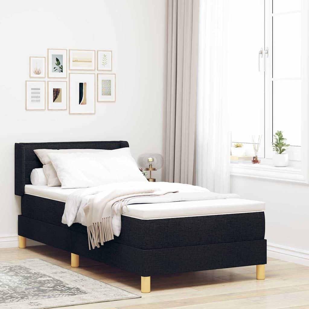 Ein sauber gemachtes Bett mit dunklem Stoffrahmen in einem hellen Raum, bestehend aus heller Bettwäsche und dekorativem Bild in Rahmen an der Wand.