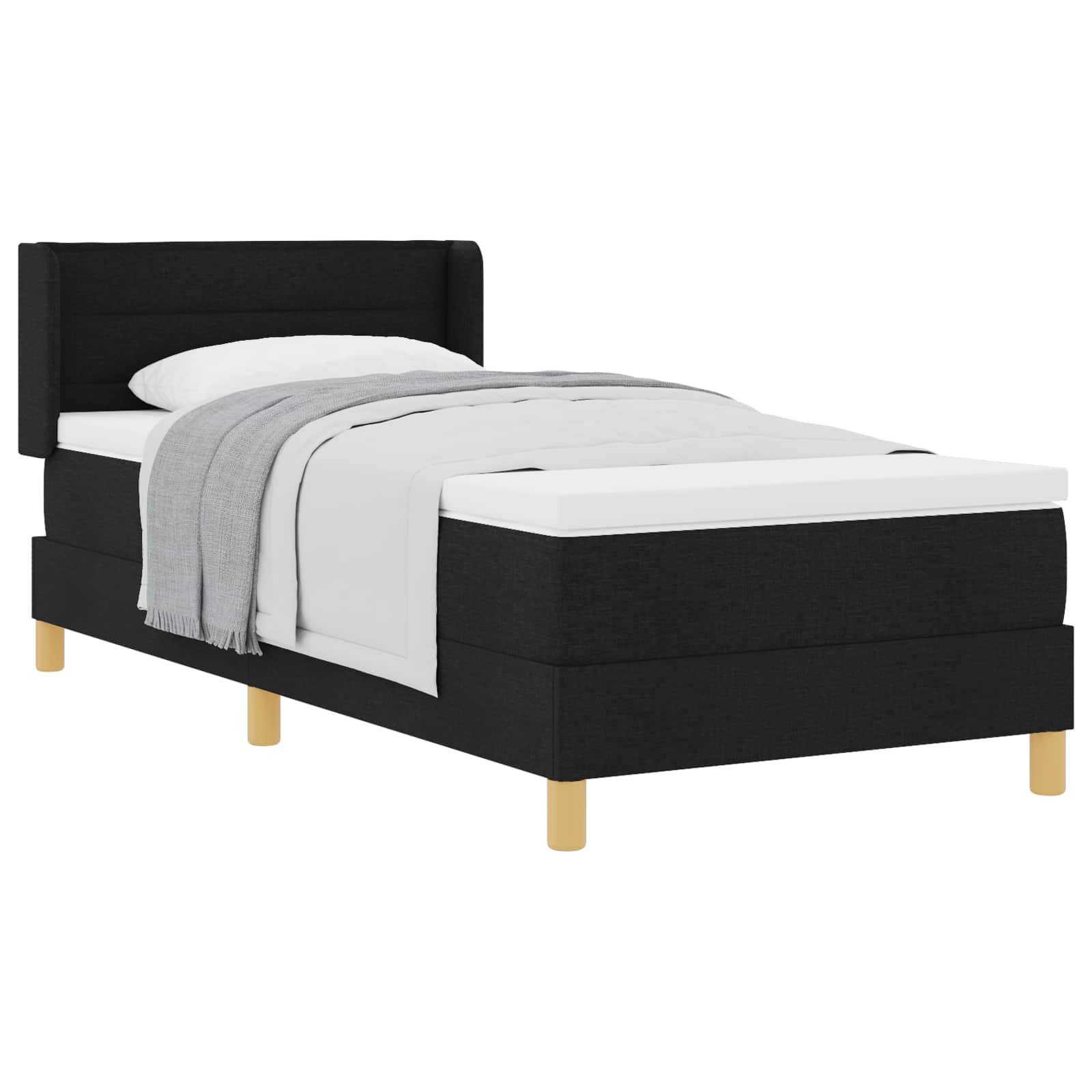 Ein einzelnes schwarzes Bett mit Kopfteil, weißer Matratze, weißem Kissen und grauer Decke. Das Bett hat Holzbeine und ein minimalistisches Design.