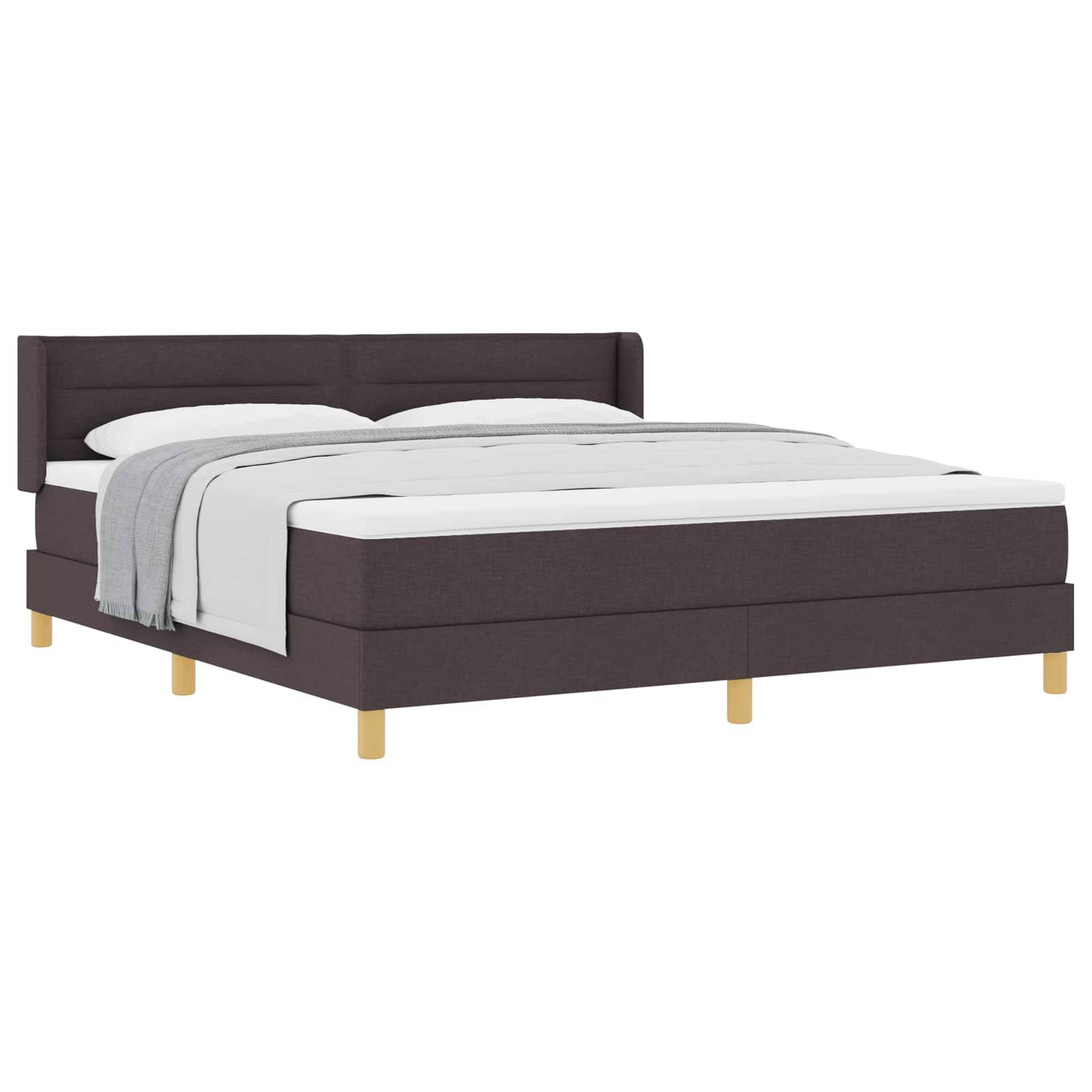 Ein modernes Bett mit dunklem Stoffrahmen und hellen Holzbeinen; es verfügt über eine weiße Matratze und gräuliche Bettwäsche.