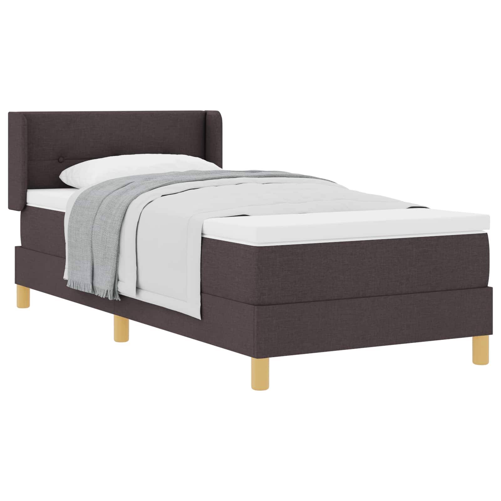 Einzelbett mit dunkelbraun gepolstertem Rahmen, weißer Bettwäsche und einer grauen Decke, die darüber drapiert ist. Helle Holzbeine bieten Stabilität.