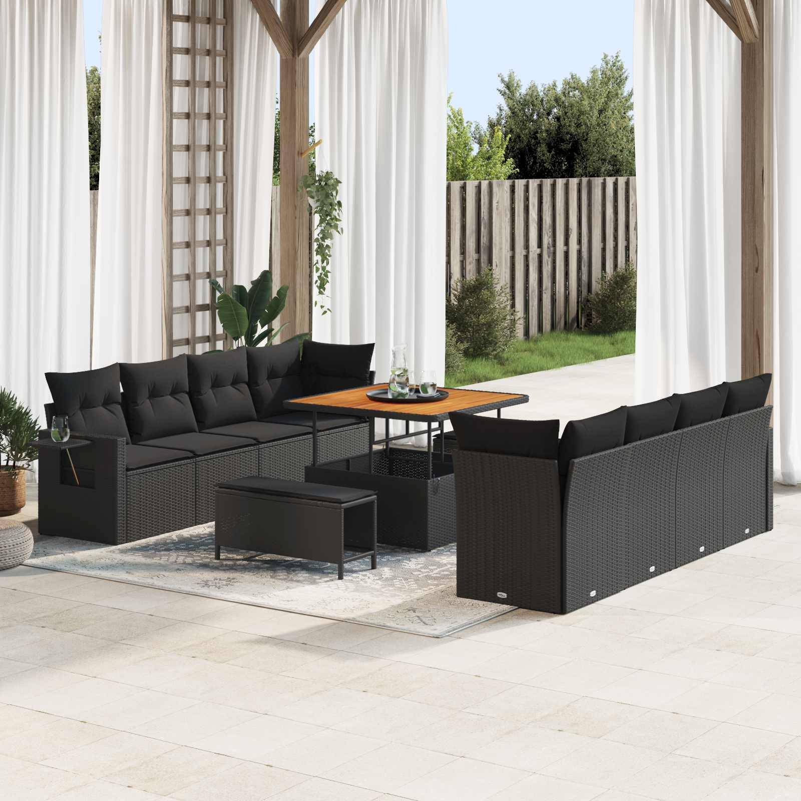 Außenterrasse mit schwarzem Polyrattan-Möbelset, bestehend aus einem Sofa, Stühlen und einem Tisch auf einem Steinfliesenboden, umgeben von Vorhängen.