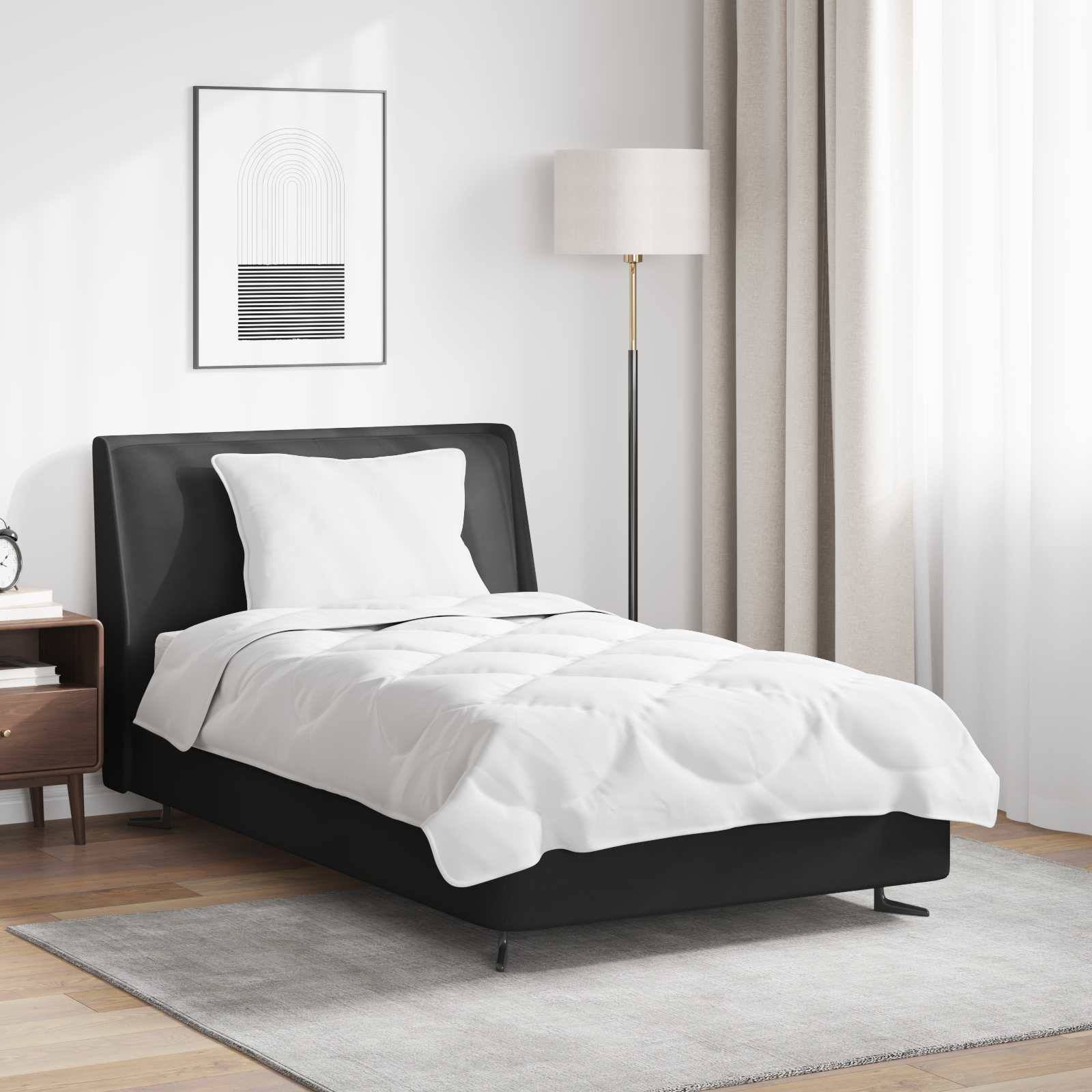 Ein ordentlich gemachtes Bett mit weißer Bettwäsche, einem schwarzen Bettrahmen und einem Kissen. Daneben ein Holznachttisch mit einer Lampe und Büchern darauf.