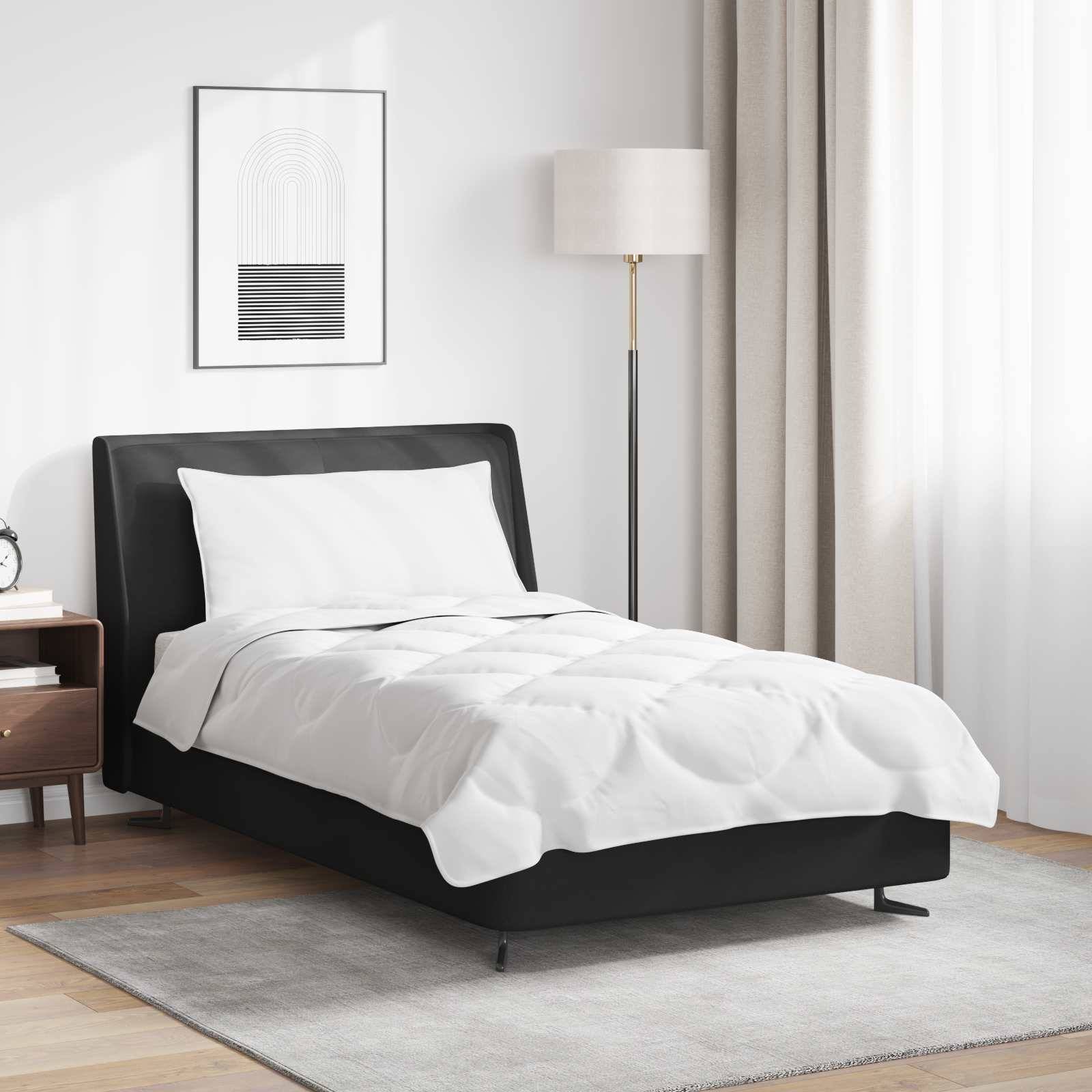 Ein sauber gemachtes Bett mit schwarzem Rahmen und weißer Bettdecke, neben einem Nachttisch und einer Stehlampe, in einem schlicht eingerichteten Raum.