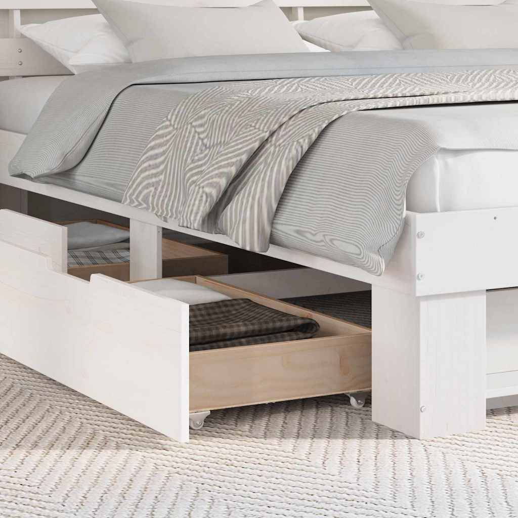 Weißes Bett mit grau gestreifter Bettwäsche und offenen Schubladen darunter, in denen eine karierte Decke liegt. Teppichboden ist sichtbar und schafft eine gemütliche Atmosphäre.