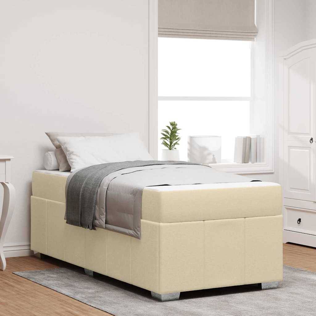 Ein ordentlich gemachtes Bett mit beiger Polsterung, einer grauen Decke und passenden Kissen befindet sich in einer hellen Ecke des Schlafzimmers mit weißen Wänden und Möbeln.