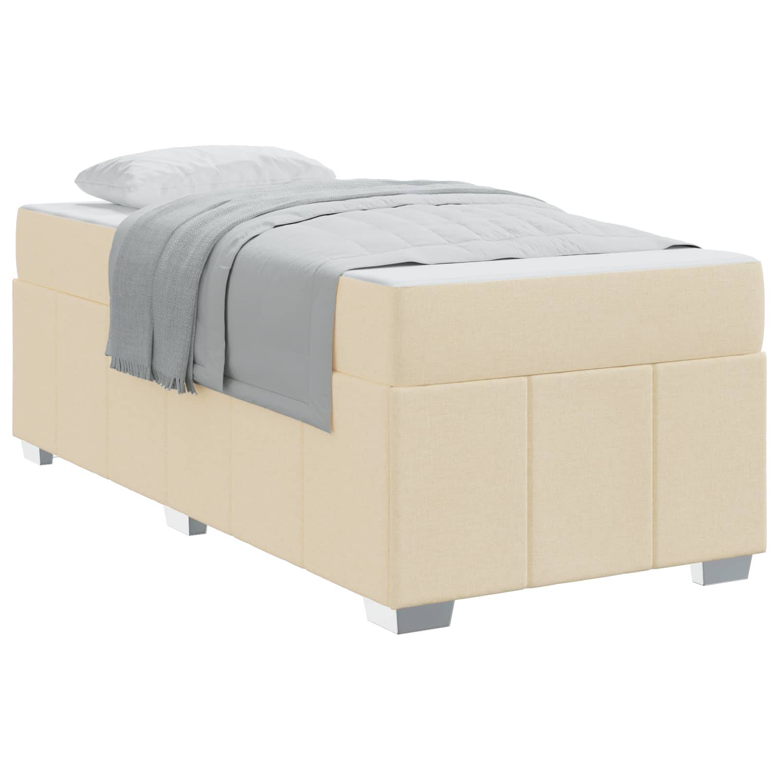 Ein beige gepolstertes Bett mit Stauraum, versehen mit einer grauen Decke und einem weißen Kissen. Auf kurzen Beinen erhöht, bietet es ein schlichtes und modernes Design.