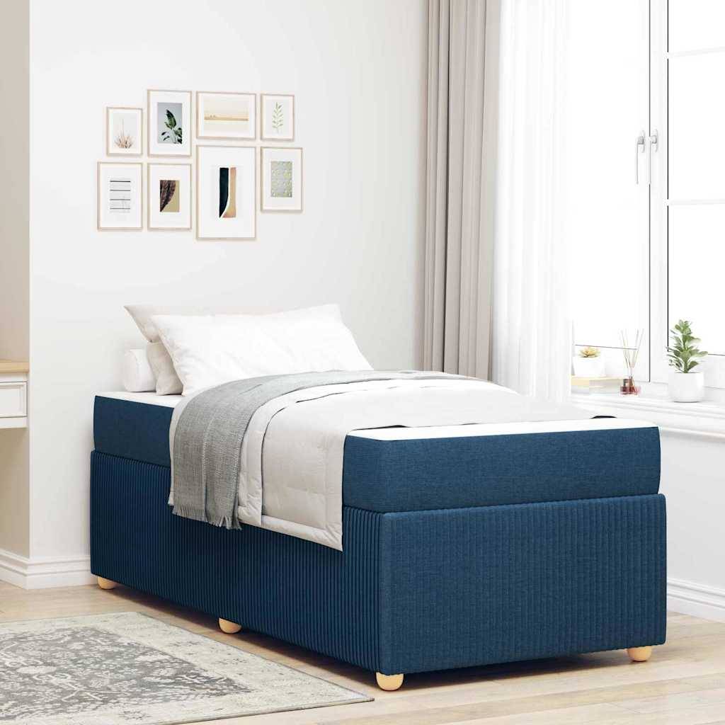 Ein modernes Schlafzimmer zeigt ein blau gepolstertes Bett mit weißer und grauer Bettwäsche, angrenzend an ein Fenster mit leichten Vorhängen und eine Wand mit Kunstwerken.