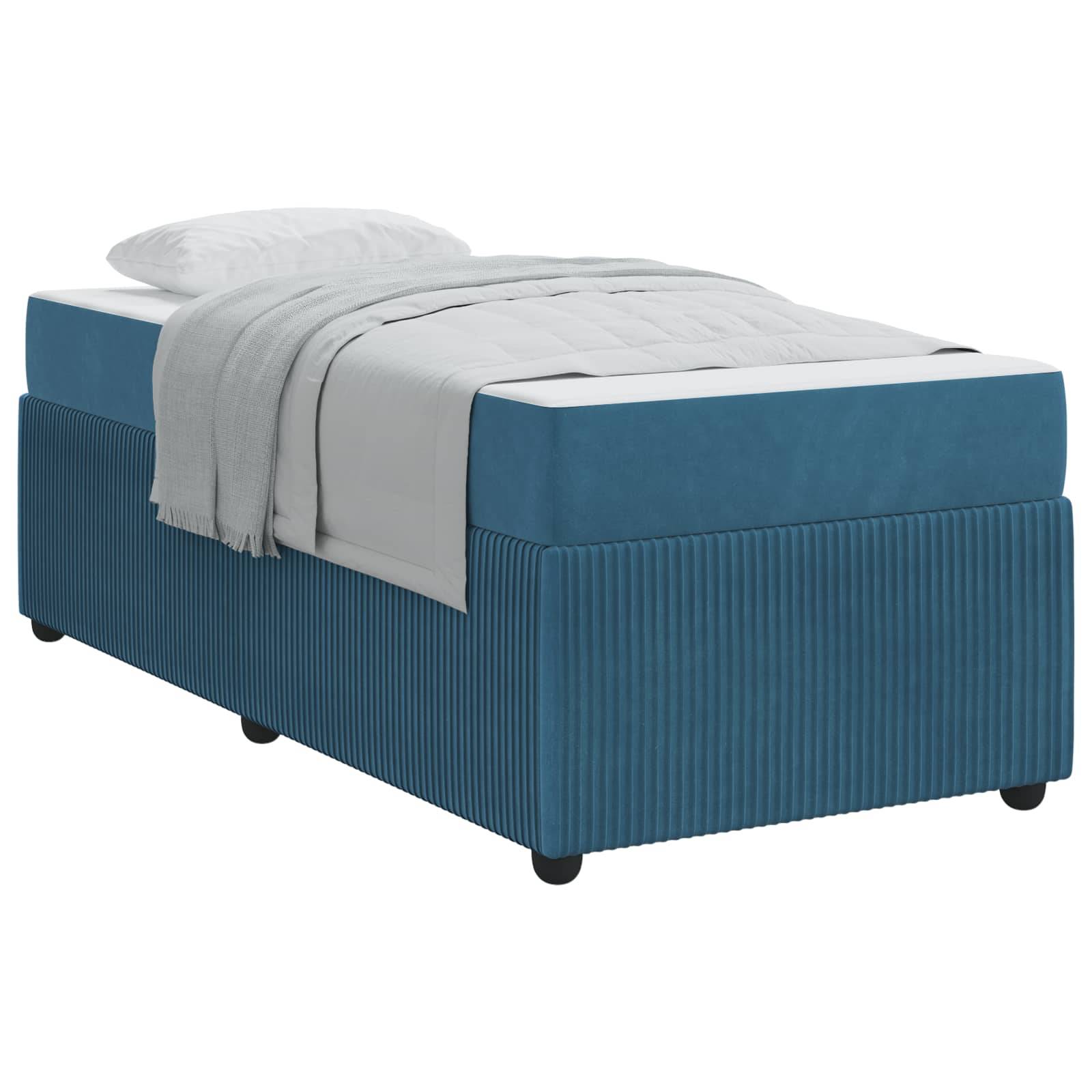 Ein blau gepolstertes Bett mit einer gerippten Basis, ausgestattet mit einer weißen Matratze und einem weißen Kissen. Das Bett hat eine grau gefaltete Decke, die teilweise darauf liegt.
