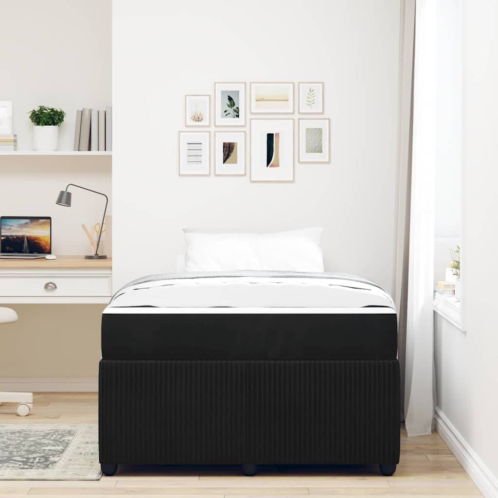 Ein ordentlich angeordnetes Schlafzimmer mit einem schwarz-weißen Bett, einem Schreibtisch links mit einer Lampe und einem Laptop sowie gerahmten Kunstwerken an den Wänden.