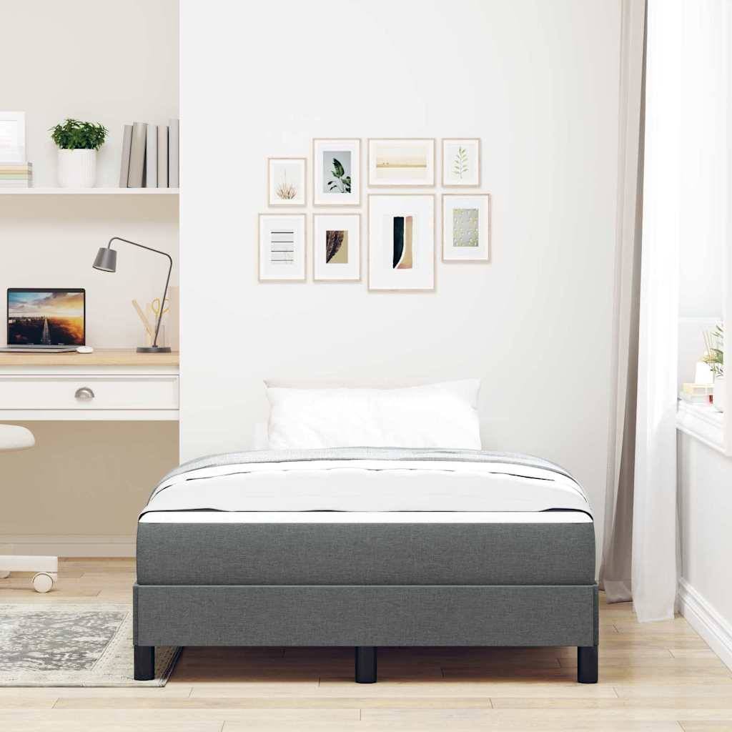 Minimales Schlafzimmer mit einem grau gepolsterten Bett, gerahmter Wandkunst und einem kleinen Schreibtisch mit Laptop und Lampe neben einem Fenster.