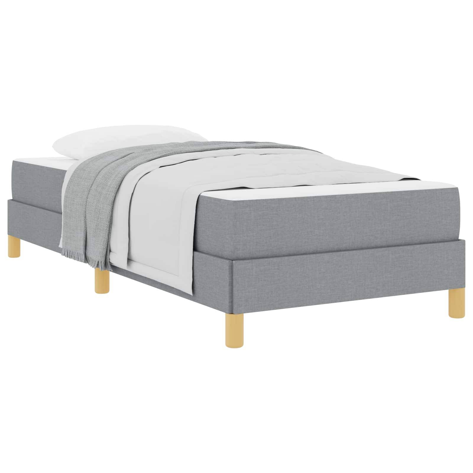 Ein graues gepolstertes Bett mit Holzbeinen, bedeckt mit weißer Bettwäsche und einer hellgrauen Decke, die über eine Seite gelegt ist.